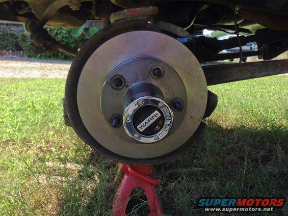 close-up of a vehicle's front wheel hub with a WARN locking mechanism, supported by a red jack stand
