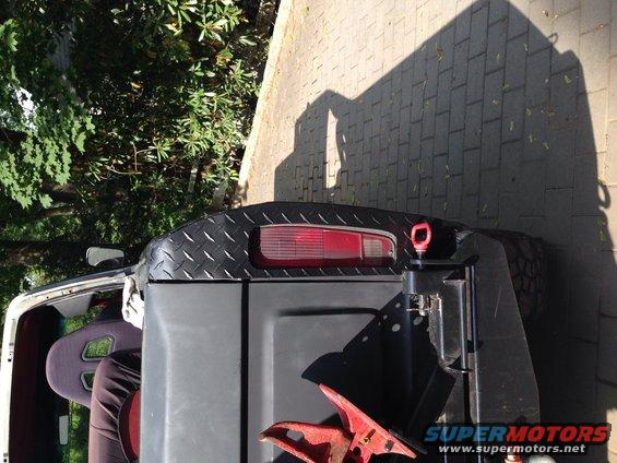 Black diamond plate tailgate with red taillight on an SUV, red tow hook visible