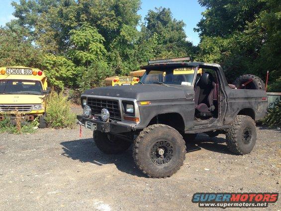 Black lifted Ford Bronco with off-road tires, parked next to yellow school buses