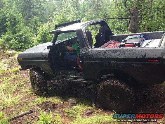 Black 1978 Ford Bronco with doors removed, off-roading in a muddy forest