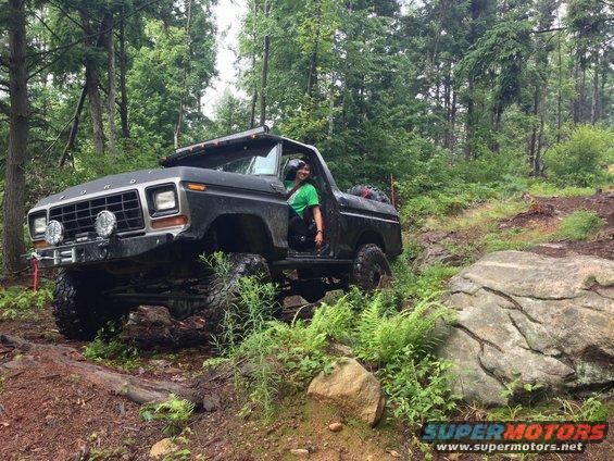Black 1979 Ford Bronco off-roading on a rocky, wooded trail