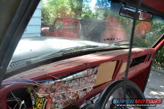 View from inside a vehicle looking out the windshield at a red Jeep Wrangler parked outside