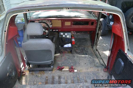 Interior of a weathered 1978 Ford Bronco, showing a red dashboard, grey seats, and a fire extinguisher
