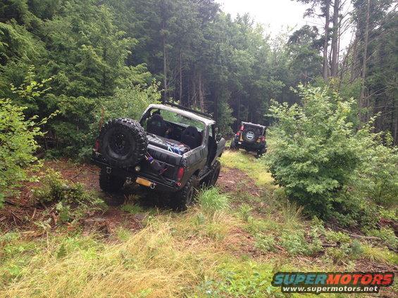 1979 Ford Bronco and a Jeep on a wooded trail. Bronco has a spare tire mounted on the rear