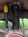 1979 Ford Bronco - Close-up of a new black coil spring and a yellow-capped shock absorber installed on a vehicle's front suspension.