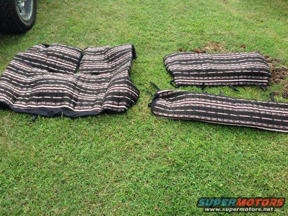 Car seat covers with a striped pattern laid out on grass. A tire and part of a vehicle are visible on the left