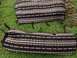 1979 Ford Bronco - Two seat covers with a black, white, and red striped pattern are laid out on the grass next to a pile of pine cones.