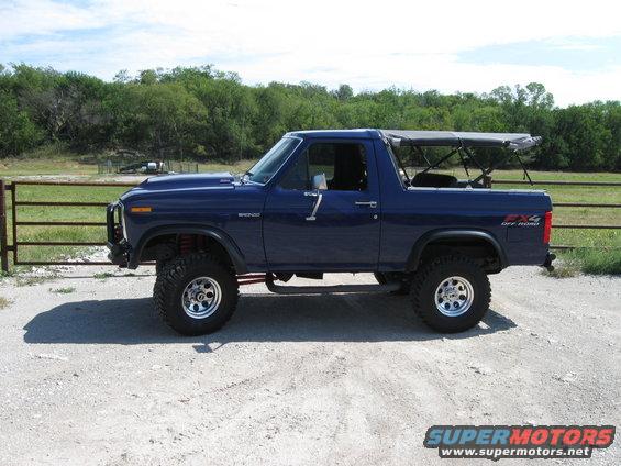 blue Ford Bronco with soft top, lifted, parked on dirt road near fence
