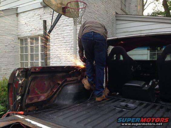 Person welding the rear of a red 1978 Ford Bronco with racing seats visible inside