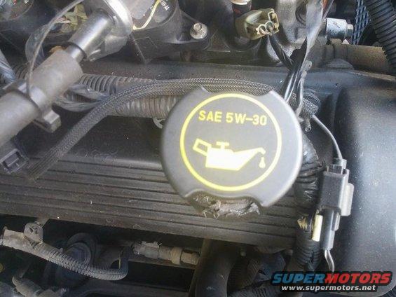 Engine bay detail showing a black oil cap with yellow SAE 5W-30 marking and oil can icon