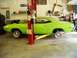 1974 Dodge Challenger - A lime green muscle car, possibly a 1970 Dodge Challenger, is elevated on a car lift in a repair shop, with its wheels removed.