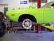 1974 Dodge Challenger - A lime green muscle car is up on a lift in a garage, showing its front suspension area.
