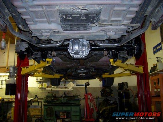 Underside of a car on a lift, showing the rear differential and exhaust system. Looks like a 2003 model
