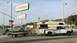 1997 Dodge 3500 - A white pickup truck tows a boat on a trailer past a gas station sign.