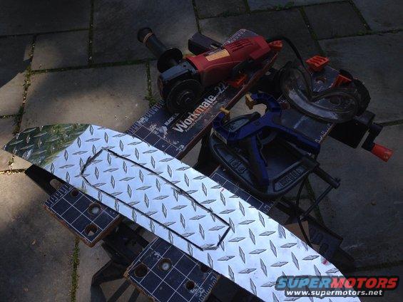 Diamond plate metal sheet with cut-out, angle grinder, and clamp on a work surface