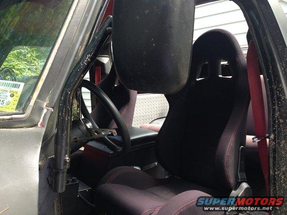 Interior of a vehicle with racing seats, roll cage, and a New York State inspection sticker on the windshield