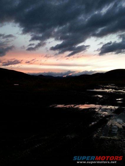 Dark landscape with puddles reflecting a colorful sunset sky