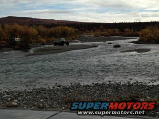 Truck crossing a shallow river with autumn trees in background