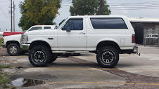 White SUV lifted on off-road tires, parked next to a red pickup truck