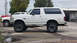 1994 Ford Bronco - Side profile of a white SUV with tinted windows and aftermarket wheels, parked outdoors.