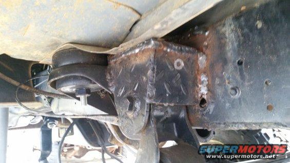 Close-up of a custom-welded suspension mount on a vehicle's frame, showing diamond plate texture and bolts