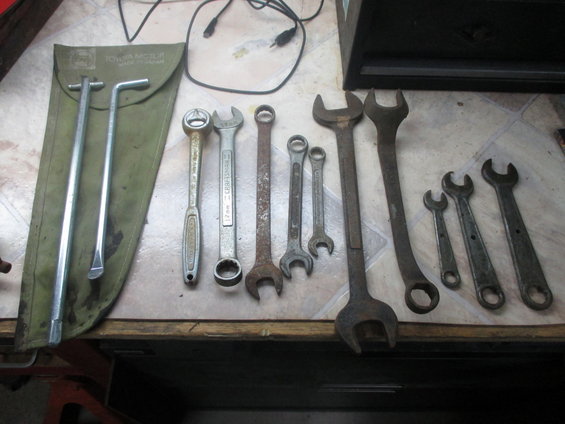 Several wrenches and a tire iron are laid out on a table. One wrench is labeled 'CRAFTSMAN 17mm'. A green pouch with two metal tools is on the left