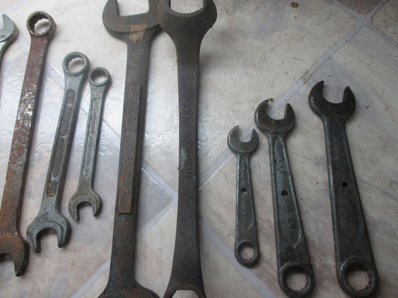 Assortment of metal wrenches of various sizes and conditions, laid out on a tiled surface