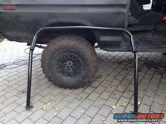 Black roll cage in front of a dark SUV's wheel and door