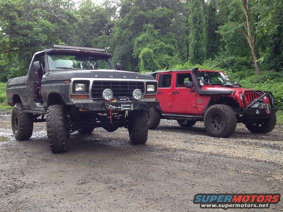 Black 1978 Ford Bronco with winch and light bar parked next to red Jeep