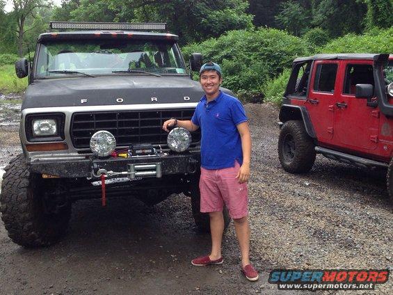 Guy next to lifted black Ford truck with winch and light bar. Red Jeep in background