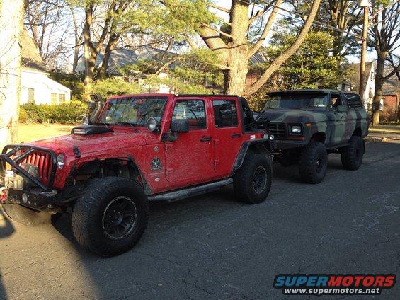 Camouflage 1979 Ford Bronco parked behind red Jeep Wrangler