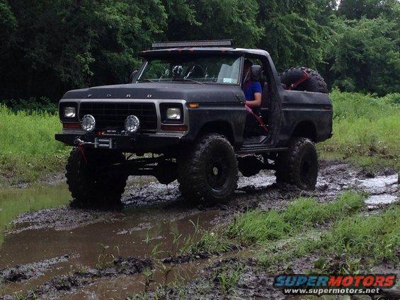 Black 1978 Ford Bronco with lifted suspension and off-road tires driving through mud