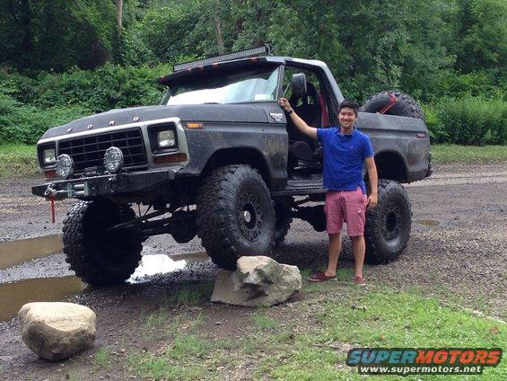 Black 1979 Ford Bronco, lifted with large tires, driver's door open, man standing beside it