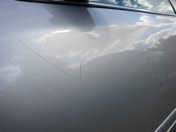 Silver car door with several long scratches. Clouds and sky reflected on the surface