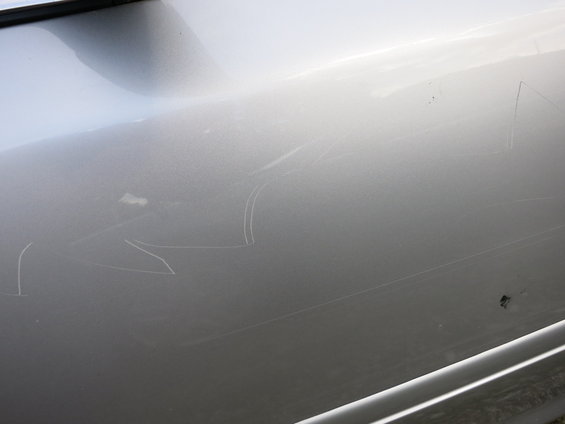 Silver car door with numerous white scratches and a small dark mark