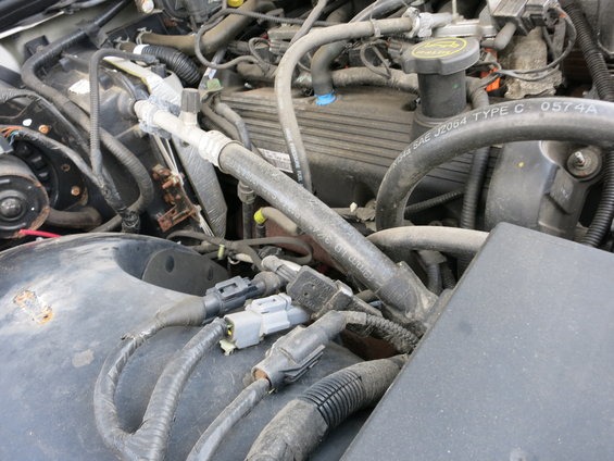 Engine bay with hoses, wires, and engine components visible. Text on a hose reads 'SAE J2064 TYPE C 0574A'