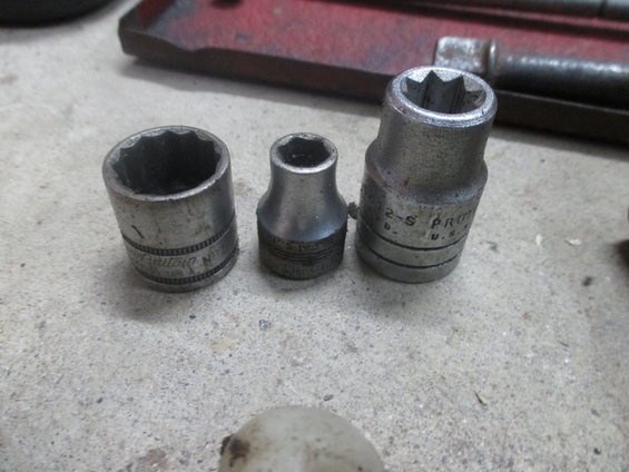 Three metal socket wrenches of varying sizes on a concrete surface
