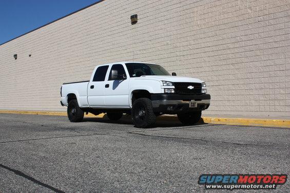 White 2006 Chevrolet Silverado 2500 pickup truck with black wheels parked in front of a beige brick wall