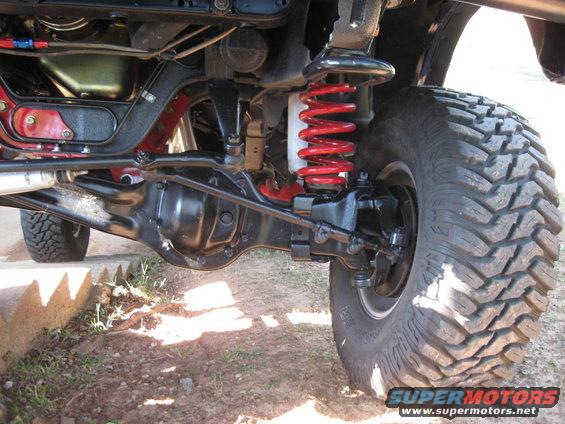 Close-up of a vehicle's front suspension and tire, showing red coil springs and a black differential