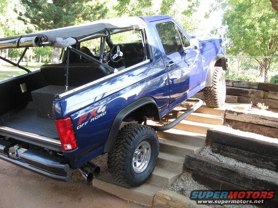 Blue 4x4 off-road SUV with custom roll cage and soft top, climbing concrete steps