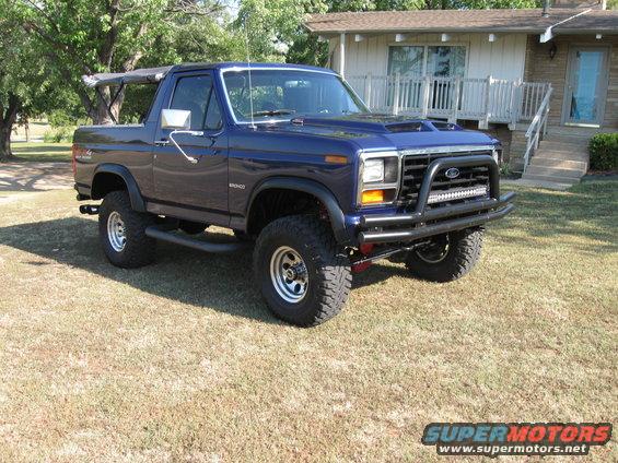 1982 Ford Bronco parked on grass in front of a house, with a custom bull bar and LED light bar
