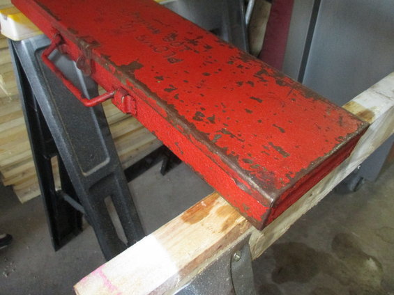 Red metal toolbox with rust spots and a handle, resting on sawhorses