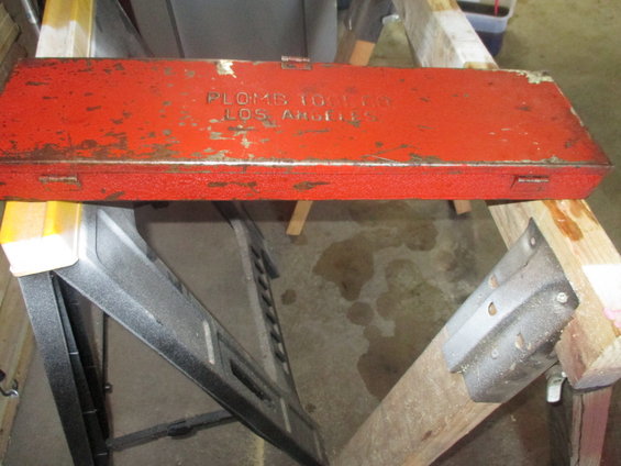 red metal toolbox with 'PLOMB TOOLS LOS ANGELES' text on top, resting on sawhorses