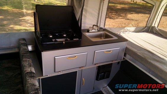 Pop-up camper kitchen area with stove and sink, next to a bed