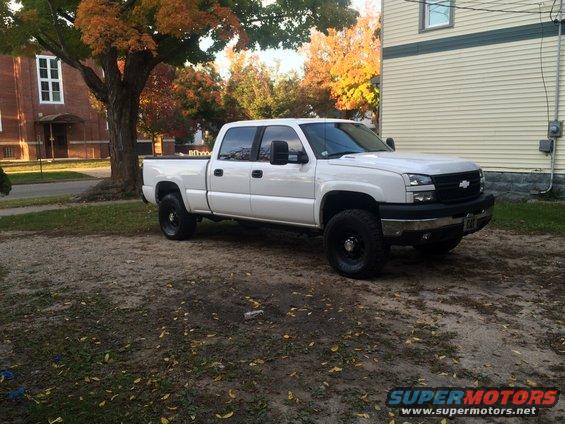 White Chevrolet Silverado pickup truck, 3/4 front view, parked on gravel with autumn leaves