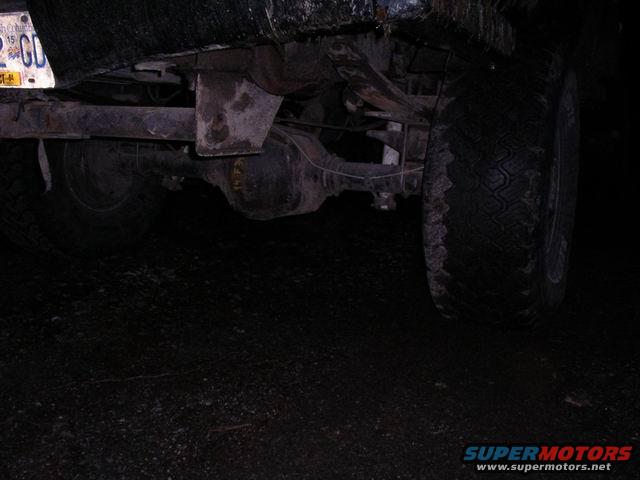 Rear axle, leaf springs, and tire of a truck. License plate visible