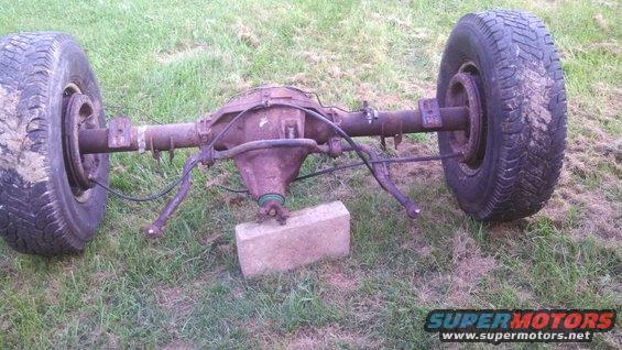 Rear axle assembly with two tires, resting on a brick, outdoors on grass