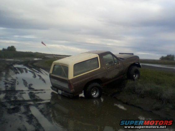 Brown and tan 1980 Ford Bronco stuck in mud, 3q-front view