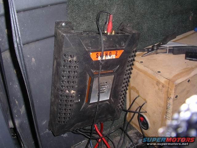 Black car stereo amplifier with orange and silver accents, connected to red and black wires