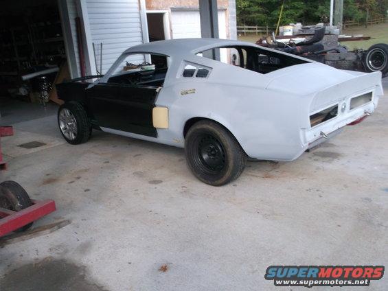 1967 Ford Mustang undergoing restoration, primer gray body with black doors, custom wheels on front, black steel wheel on rear